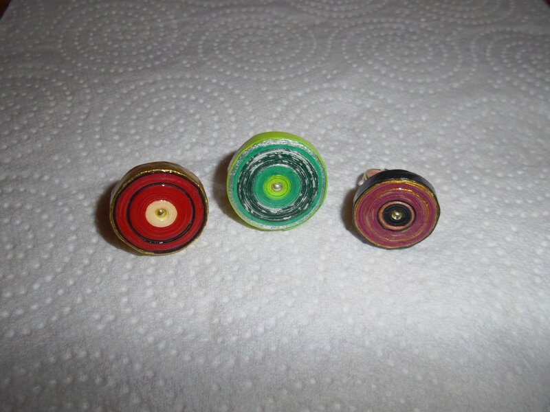 Trois anneaux de papier en spirale aux couleurs vives, rouge, vert et rose, posés sur une surface claire et texturée, ambiance artisanale et joyeuse
