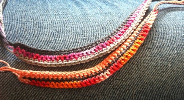 Deux bracelets en crochet multicolores, orange, rose, rouge et gris, posés sur un tissu denim bleu, tons chauds et artisanat coloré