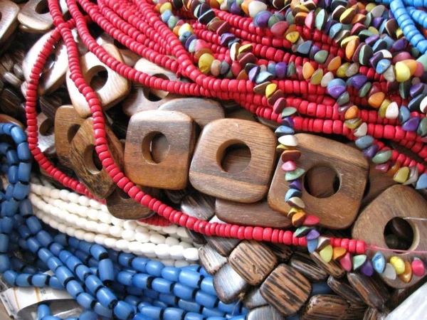 Tas de colliers de perles de bois et de perles colorées en rouge, bleu et blanc, rendu facetté aux tons chauds, ambiance artisanale